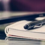 Close-up of an elegant pen resting on an open notebook in a stylish office environment.